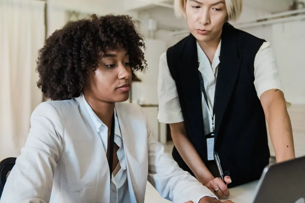 A mentor guiding a colleague at a laptop