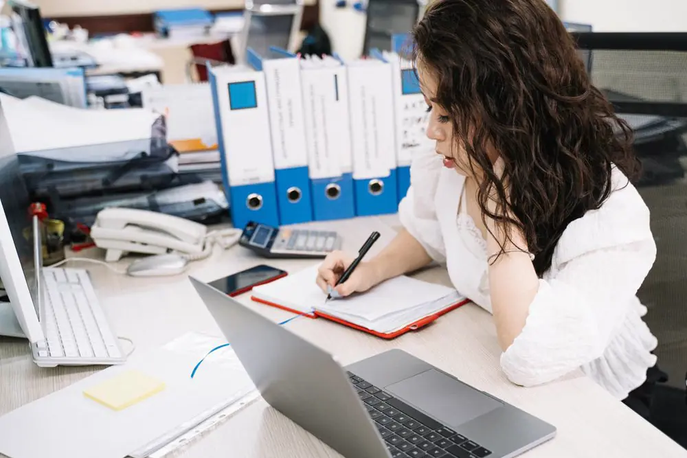 A woman writing notes at an office desk